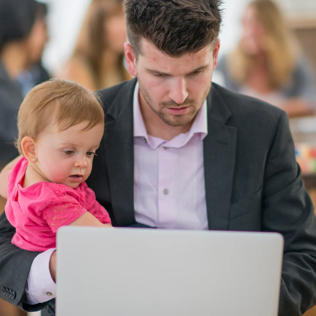 Man in a suit holding a young child on his lap while they both look at a laptop screen.