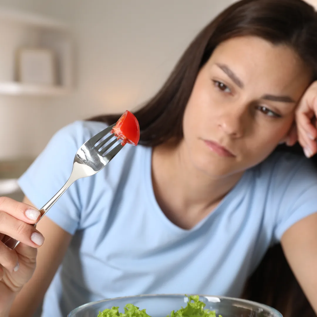 Person holding a fork with a small tomato over a bowl of lettuce, appearing hesitant to eat it.