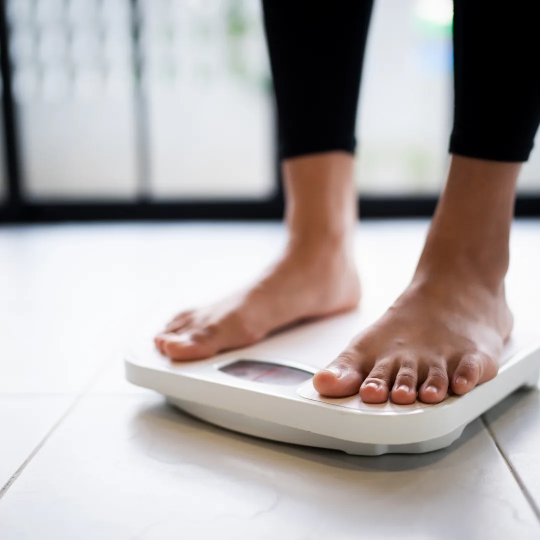 Bare feet standing on a white bathroom scale on a tiled floor