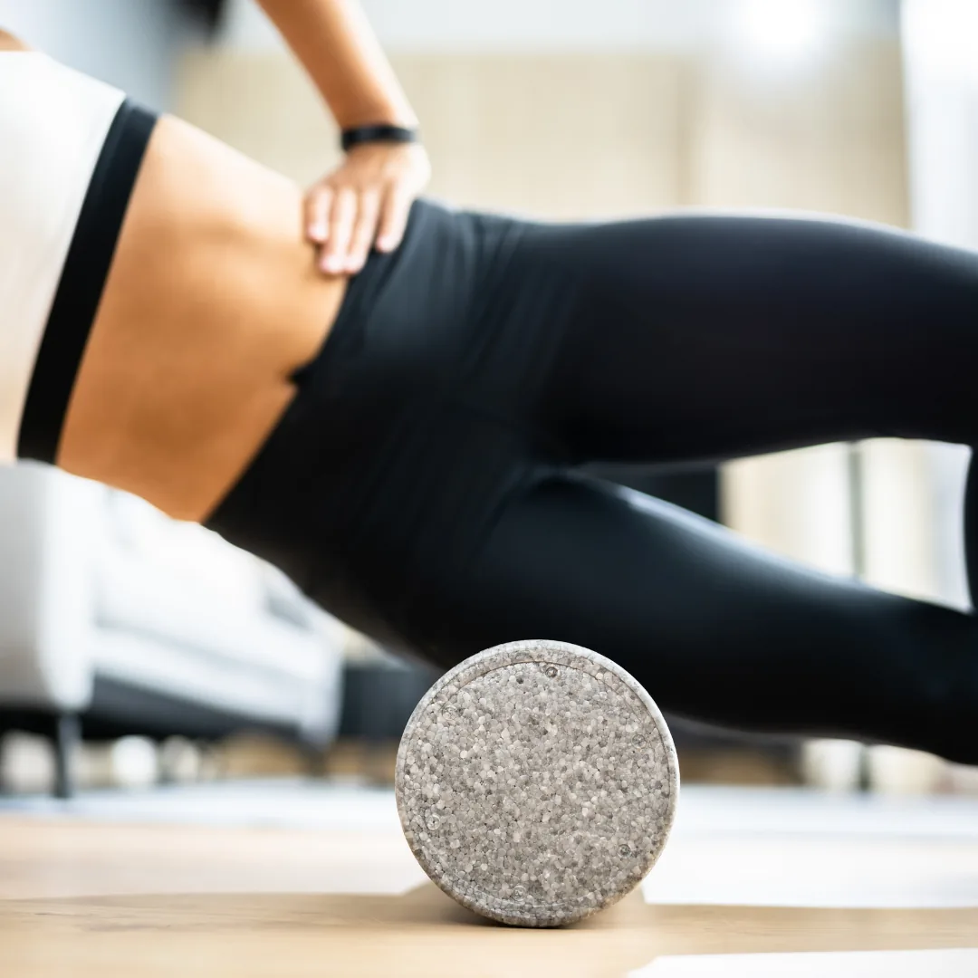 Person in a side plank position using a foam roller under the outer hip/glute on a hardwood floor.