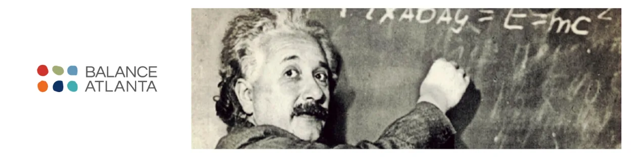 Person with disheveled hair writing the equation E=mc² on a chalkboard, glancing back toward the camera.