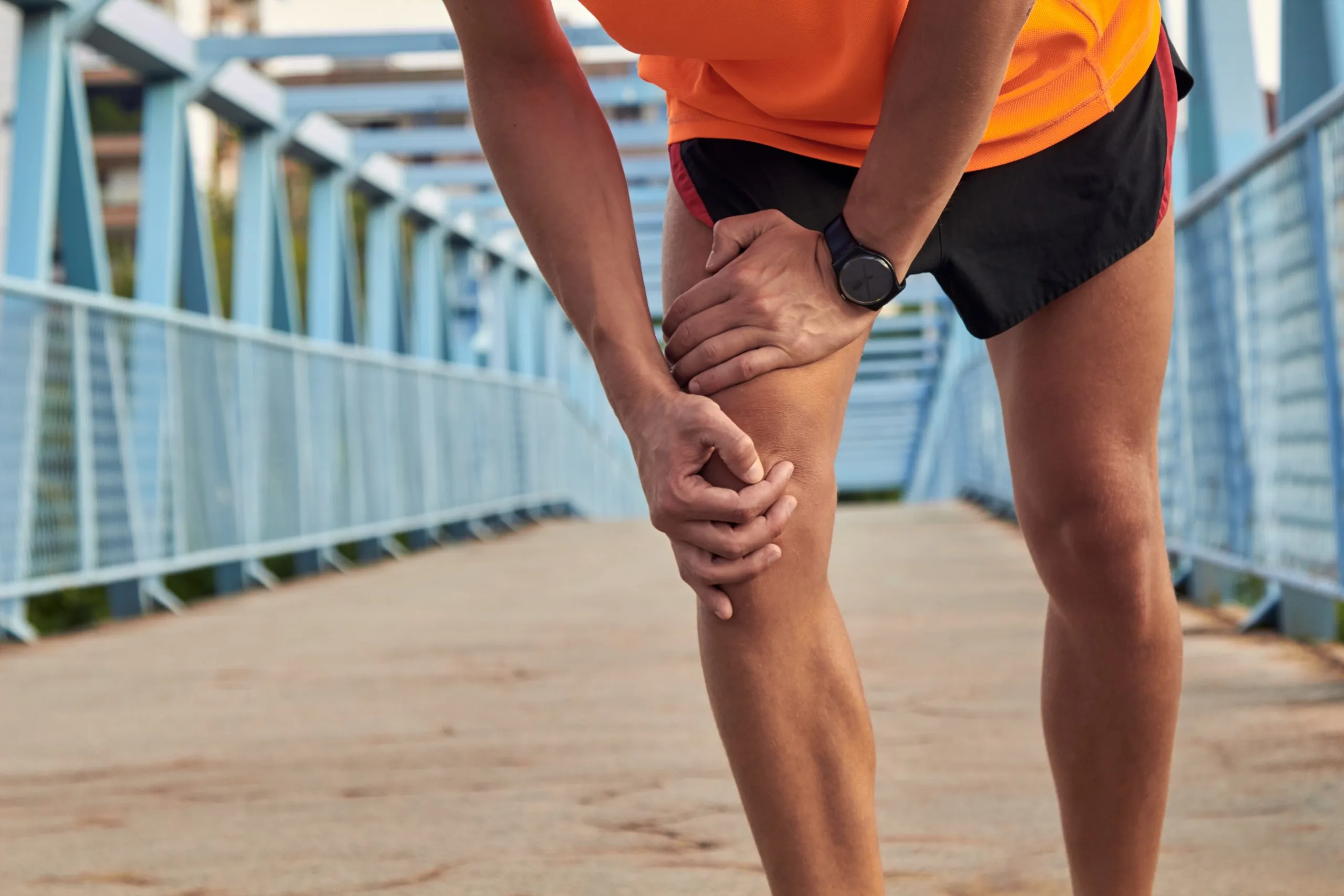 Runner clutching their knee and lower thigh while standing on a pedestrian bridge