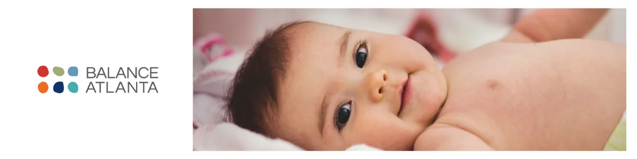 Smiling baby lying on a blanket with torso and face visible, looking toward the camera