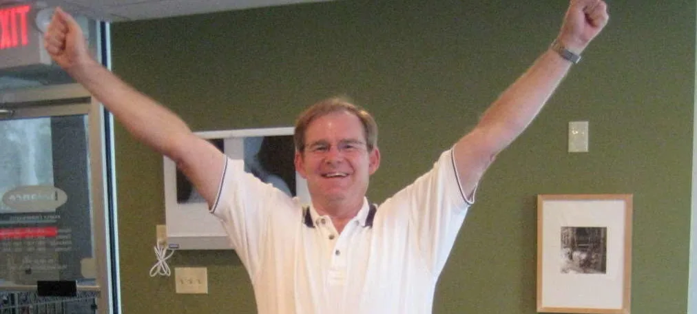 Smiling man indoors with both arms raised above his head