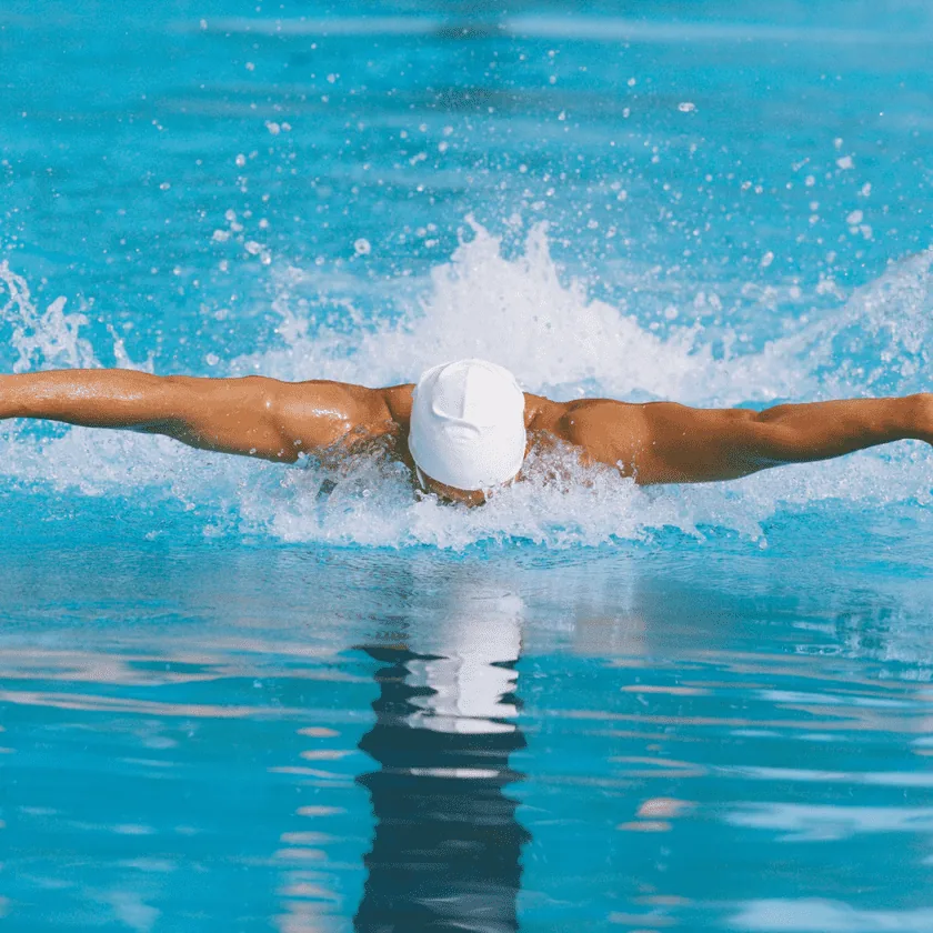 Swimmer performing the butterfly stroke in a pool, arms outstretched and water splashing behind them.
