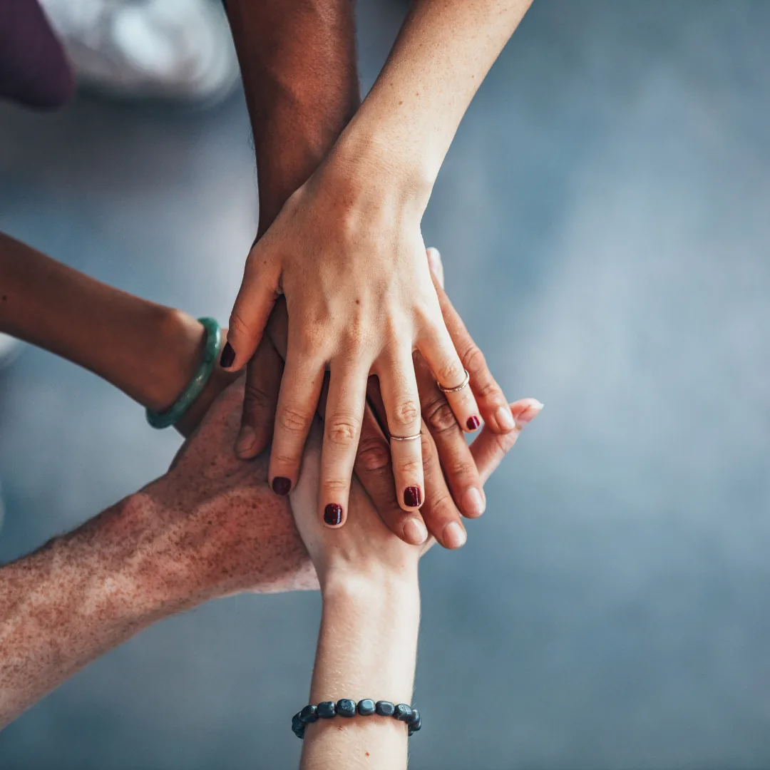 Multiple hands stacked together in a group, symbolizing support and teamwork.