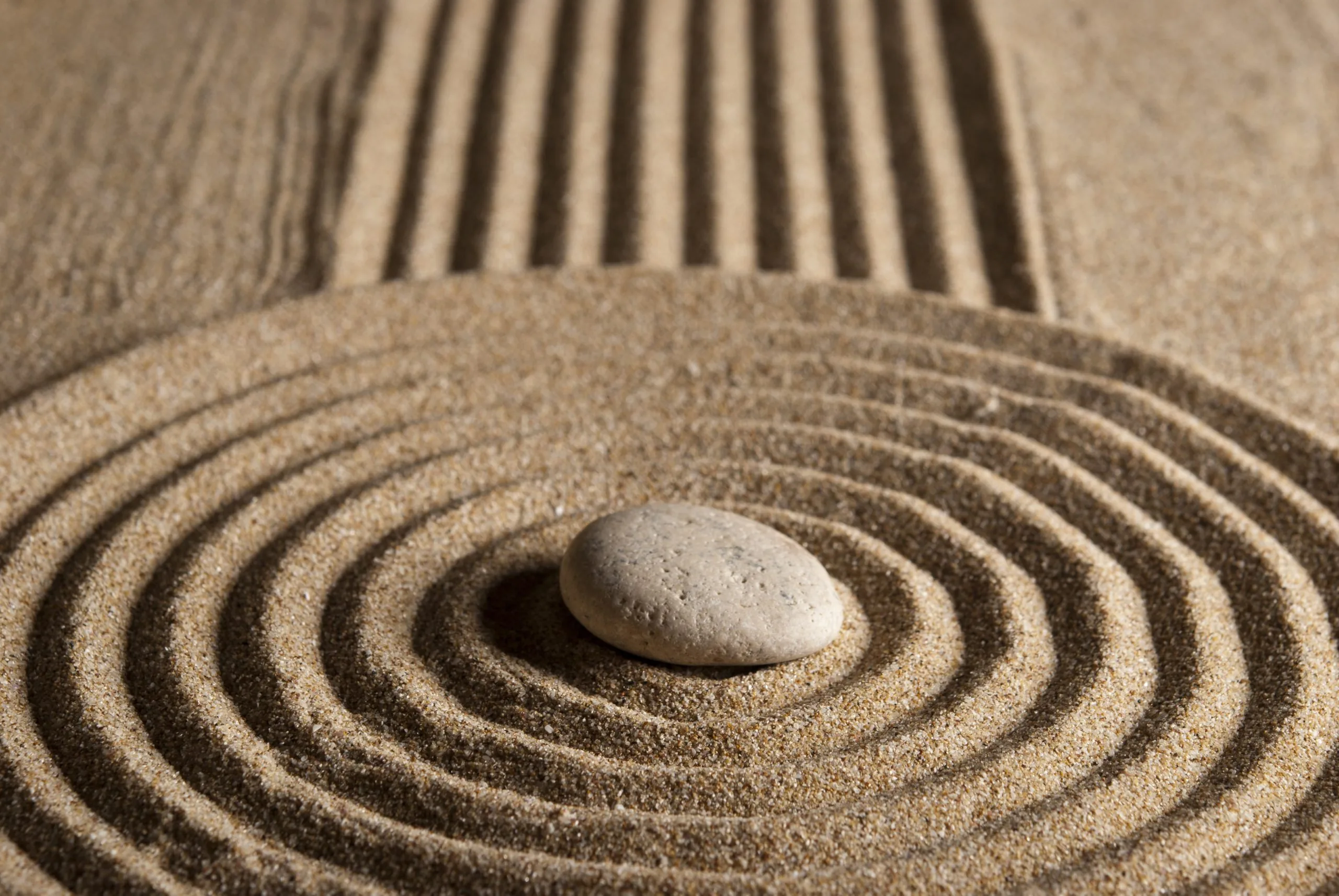 Smooth round stone centered in raked sand with concentric circular grooves