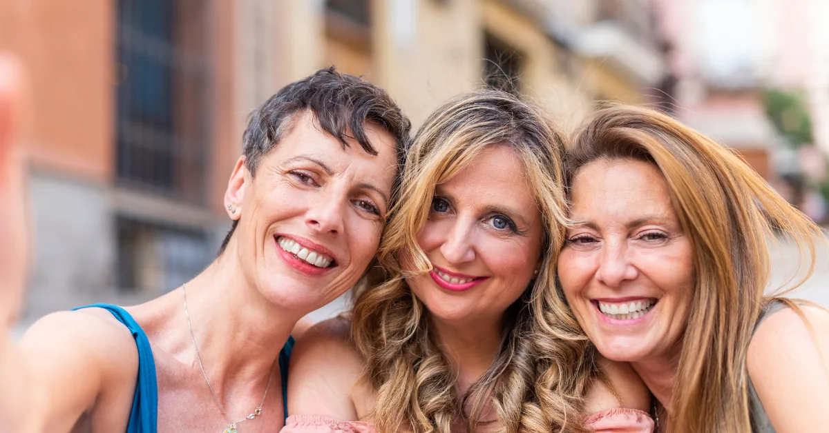 Three smiling women posing closely together for a selfie outdoors