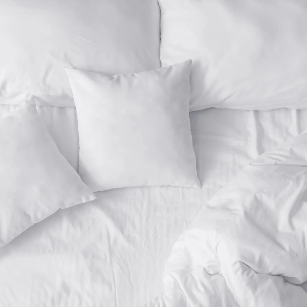 Top-down view of white pillows and rumpled bedding on a bed.