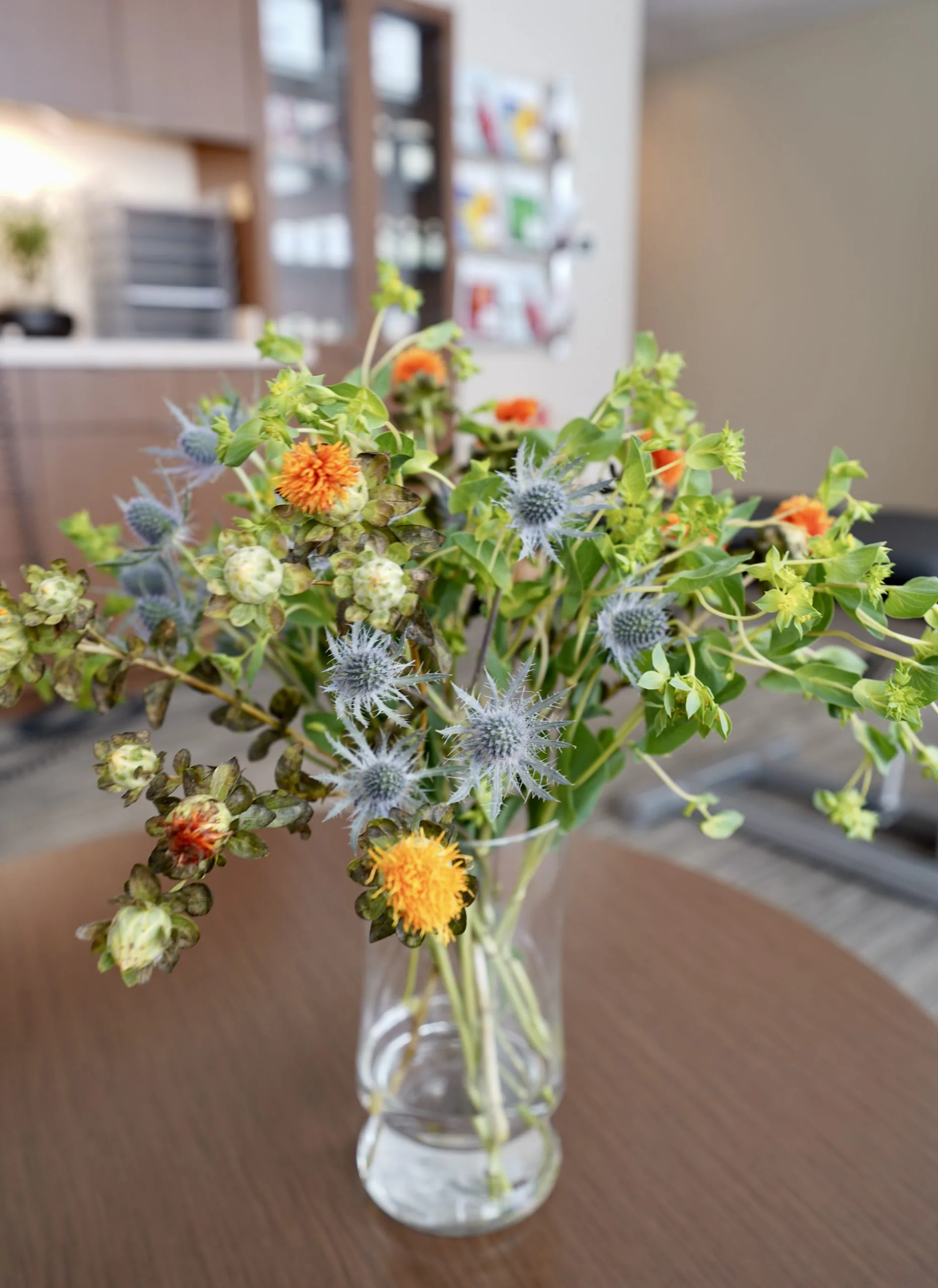 Vase of orange and blue wildflowers on a table with a blurred reception area in the background.