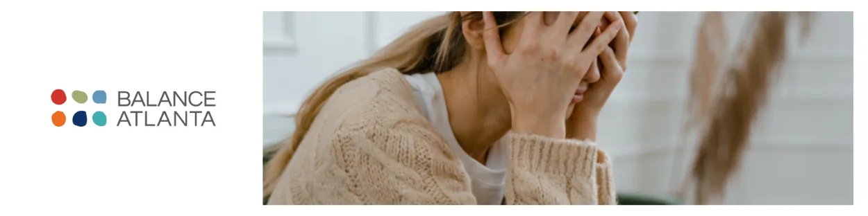 Woman sitting with hands covering her face, wearing a knit sweater; Balance Atlanta logo at left.