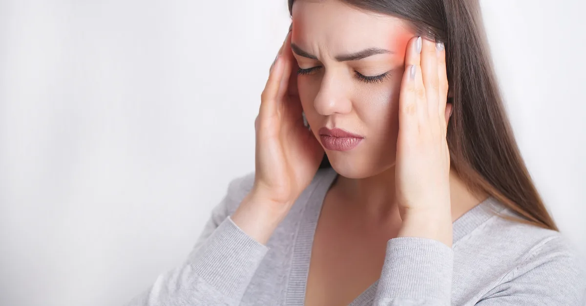 Woman pressing her temples with eyes closed and a pained expression, red highlights at the temples indicating head pain